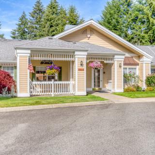A charming residential house with a front porch adorned with hanging flowers, surrounded by lush greenery and a driveway.