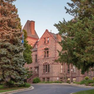 A historic gothic-style brick building surrounded by lush trees and a winding road.