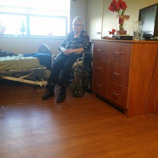 An elderly person in a wheelchair sitting in a nursing home room.
