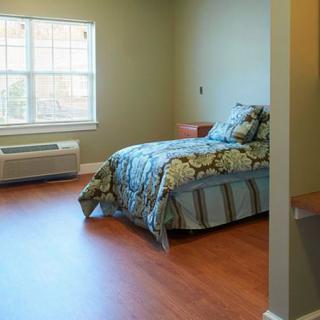 A simple, neatly arranged bedroom with a bed near a large window and wood flooring.