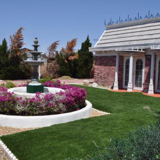 A landscaped garden with a circular flower bed and fountain adjacent to a brick building.