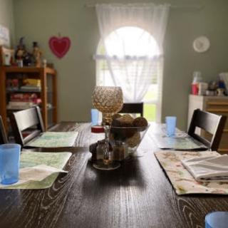 A cozy dining room with a set table, featuring placemats and glasses, softly lit by natural light from the window.