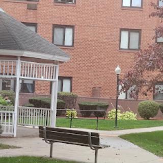A peaceful outdoor area featuring a bench and gazebo near an apartment building.