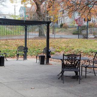 An outdoor patio area with chairs and a table under a pergola, surrounded by autumn foliage.