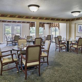 A well-arranged dining room with multiple tables and chairs, featuring carpeted flooring and soft ceiling lighting.
