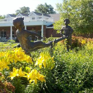 Bronze sculptures of children playing in a garden with yellow flowers.