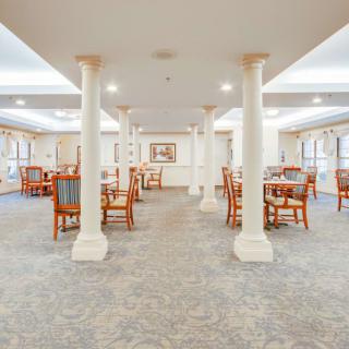 Elegant dining area with tables and chairs, featuring columns and carpeted flooring.