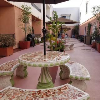 A cozy courtyard with mosaic tables and benches, surrounded by potted plants and shaded by umbrellas.