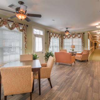 A cozy seating area with comfortable chairs and tables, well-lit by large windows and enhanced with wooden flooring and ceiling fans.
