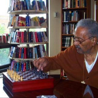 An elderly person playing chess in a library setting.