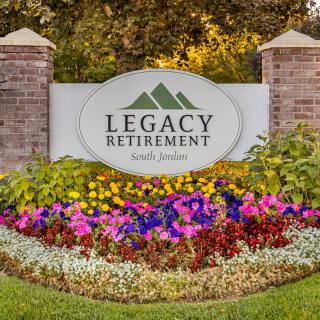 Entrance sign to Legacy Retirement surrounded by colorful flowers and landscaping.