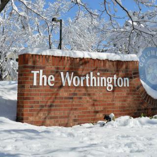 A brick sign for 'The Worthington' covered in snow during winter.