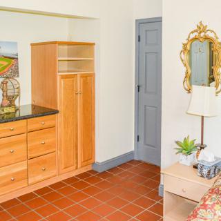 A cozy bedroom interior featuring a wooden dresser, a decorative mirror, and a bedside table with a lamp and plant.