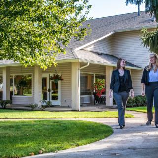 Two people walking on a pathway in front of a house surrounded by greenery.