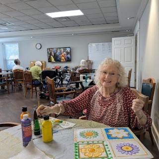 An elderly woman engages in a creative painting activity at a community center, surrounded by fellow participants.