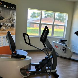A gym room featuring exercise equipment including a recumbent bike and cardio machines, with a window providing natural light.