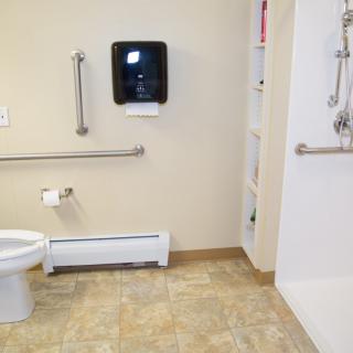 An accessible bathroom featuring grab bars, a toilet, and a shower area.