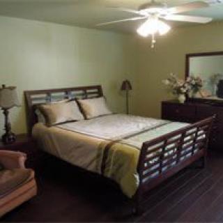 A modern bedroom with a wooden bed frame, matching dresser and mirror, and a ceiling fan.