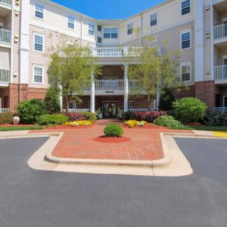 A view of a multi-story apartment building with well-maintained landscaping at the entrance.