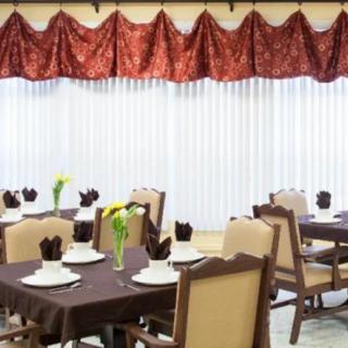 A dining room setup with neatly arranged tables and chairs, featuring elegant place settings and decorative curtains.