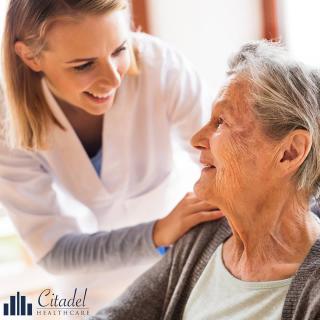 A caregiver smiling at an elderly woman, providing support and care.