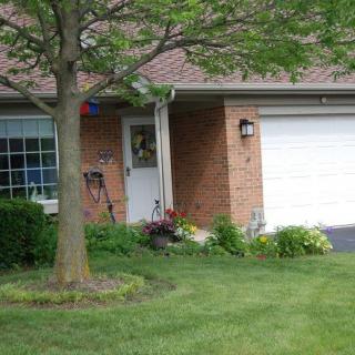 A suburban house with a well-maintained front yard, featuring a tree, green lawn, and brick exterior.