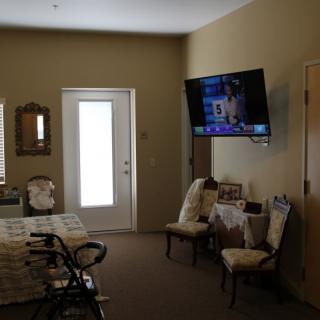 A cozy living room with a wall-mounted television, two chairs, and a small table near the door.