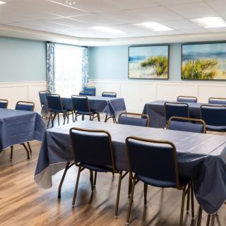 A neatly arranged meeting room with tables covered in blue tablecloths and chairs, featuring coastal artwork on the walls.
