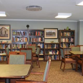 A quiet library with shelves full of books and several tables and chairs arranged for reading.
