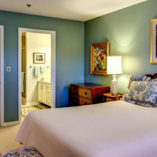 A cozy bedroom with a neatly made bed, soft lighting from a lamp, and tasteful decor including paintings and furniture.