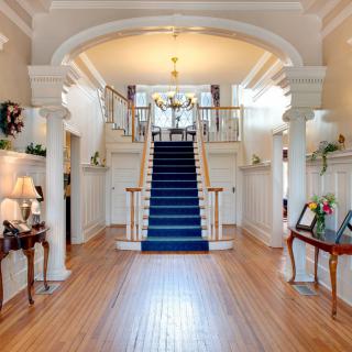 Elegant hallway featuring a grand staircase with blue carpeting and classic decor.