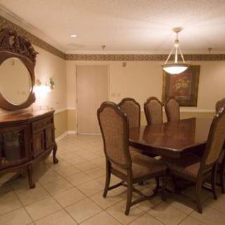 A dining room with a wooden table and upholstered chairs, featuring a chandelier and an ornate mirror on the wall.