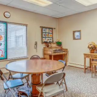 A cozy room with a round table, folding chairs, and a piano near the window.