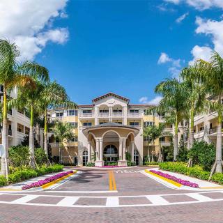 A luxurious hotel entrance surrounded by palm trees and vibrant landscaping under a bright blue sky.