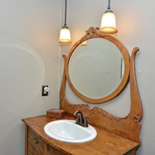 A bathroom vanity with an ornate wooden mirror and a sink, flanked by two pendant lights.