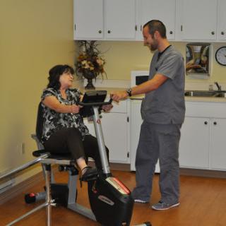 A healthcare professional assists a patient during a physical therapy session on an exercise bike.