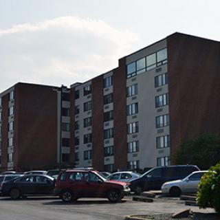 A view of a multi-story apartment building with a parking lot filled with cars.
