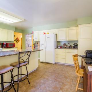 A spacious kitchen with cream-colored cabinets, bar stools at the counter, and various appliances.