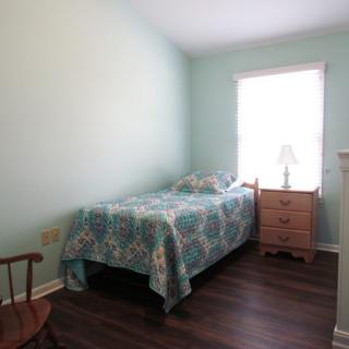 A simple bedroom with a single bed, nightstand, and wooden chair by the window.
