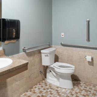 A clean and accessible public bathroom with a toilet, sink, and handrails.