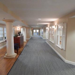 A long hallway with carpeted flooring, columns, and windows on the side.