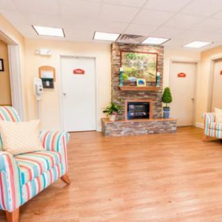 A cozy waiting room with colorful chairs and a fireplace, featuring hardwood floors and decorative elements.