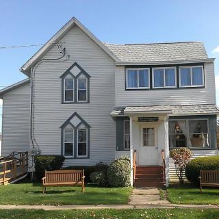 A residential house with a gabled roof and multiple windows in a grassy yard.