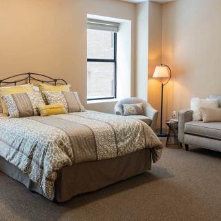 A cozy bedroom with a neatly made bed, a lamp, and a comfortable chair by the window.