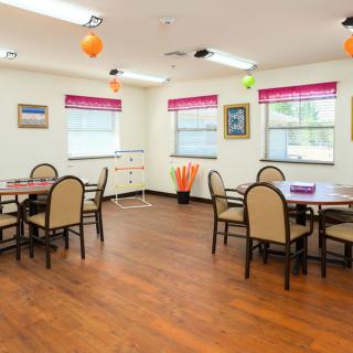 A well-lit dining area with several tables and chairs, featuring bright decor and wooden flooring.
