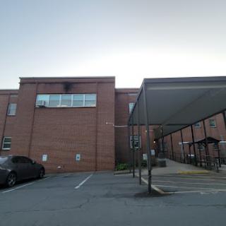 A view of a brick building with a parking area in front.