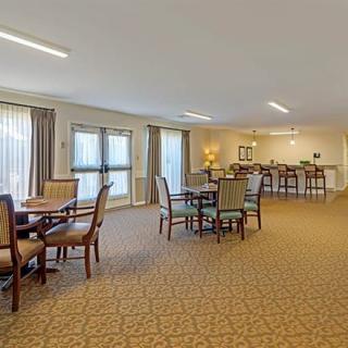 Spacious dining area with tables and chairs, featuring carpet and natural lighting.