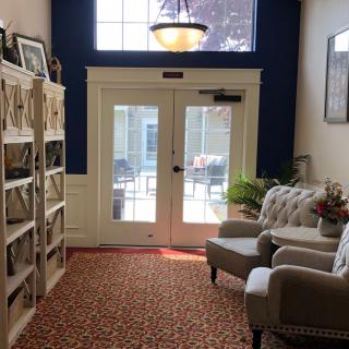 A cozy interior space featuring a seating area with armchairs, a bookshelf, and a large windowed door leading outside.