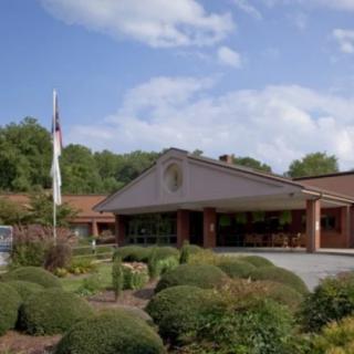 A building with a landscaped entrance, surrounded by greenery and under a partly cloudy sky.