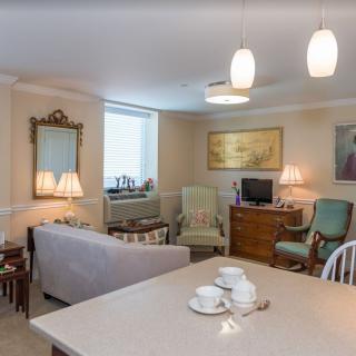 A cozy living room with classic decor featuring a sofa, chairs, and table under soft lighting.